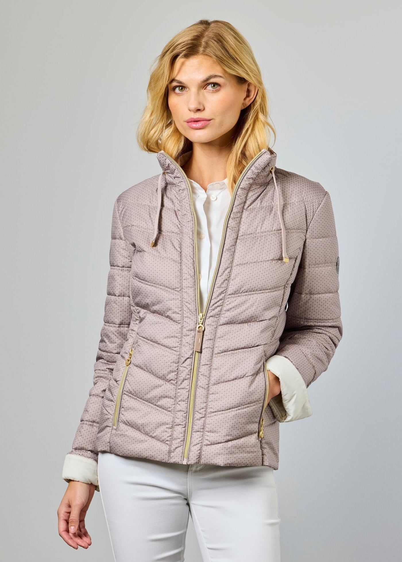 Woman wearing a light brown quilted jacket on a gray background