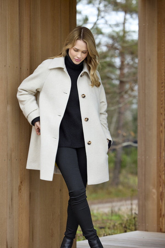 Cream wool blend coat with large buttons and raglan sleeves, worn open over black turtleneck