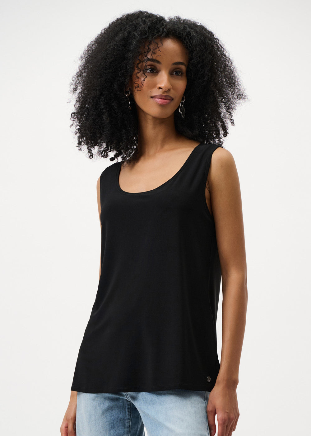 Woman wearing a black sleeveless top and light blue jeans on a white background