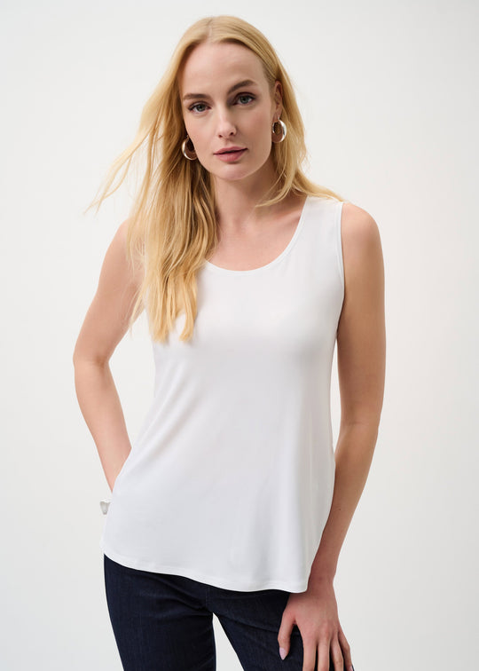 Woman wearing a white sleeveless top and dark pants on a plain background