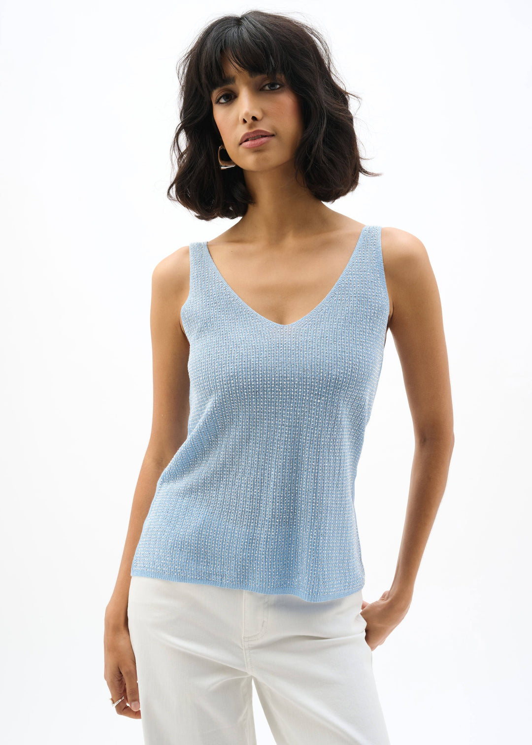 Woman wearing a light blue sleeveless top and white pants on a white background