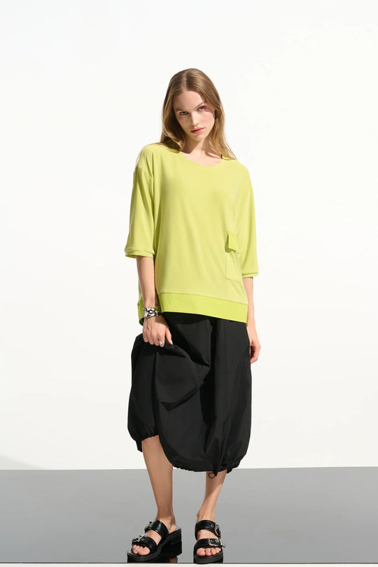 Bright green boxy tunic with three-quarter sleeves and front pocket paired with black cropped pants