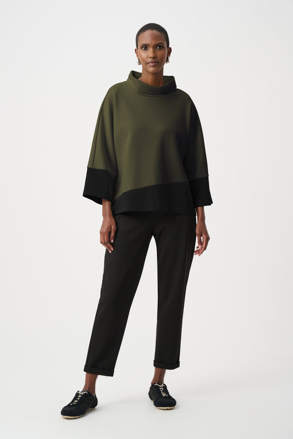Color block trapeze top with cowl neck in olive green and black worn with black pants