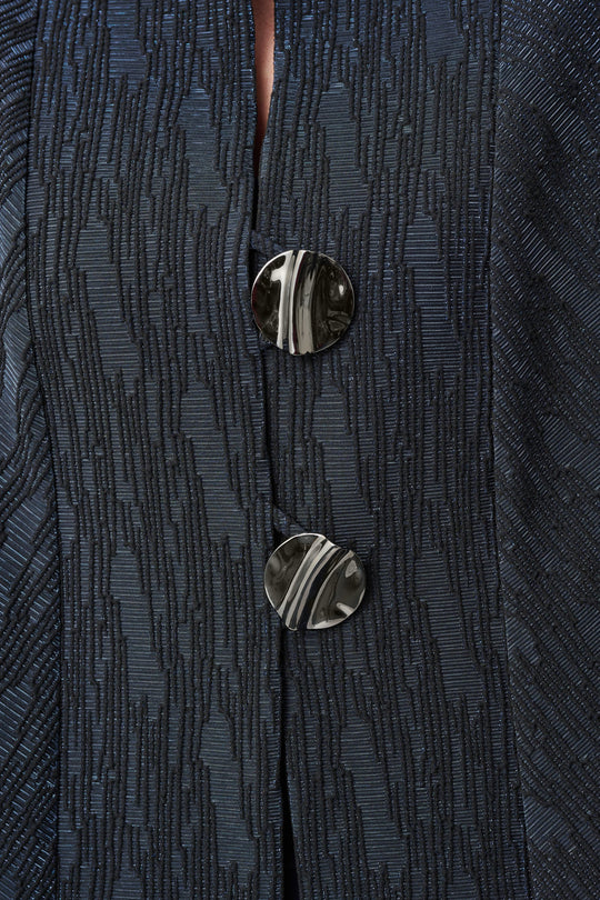 Navy textured jacquard jacket detail showing two metallic buttons and fabric pattern