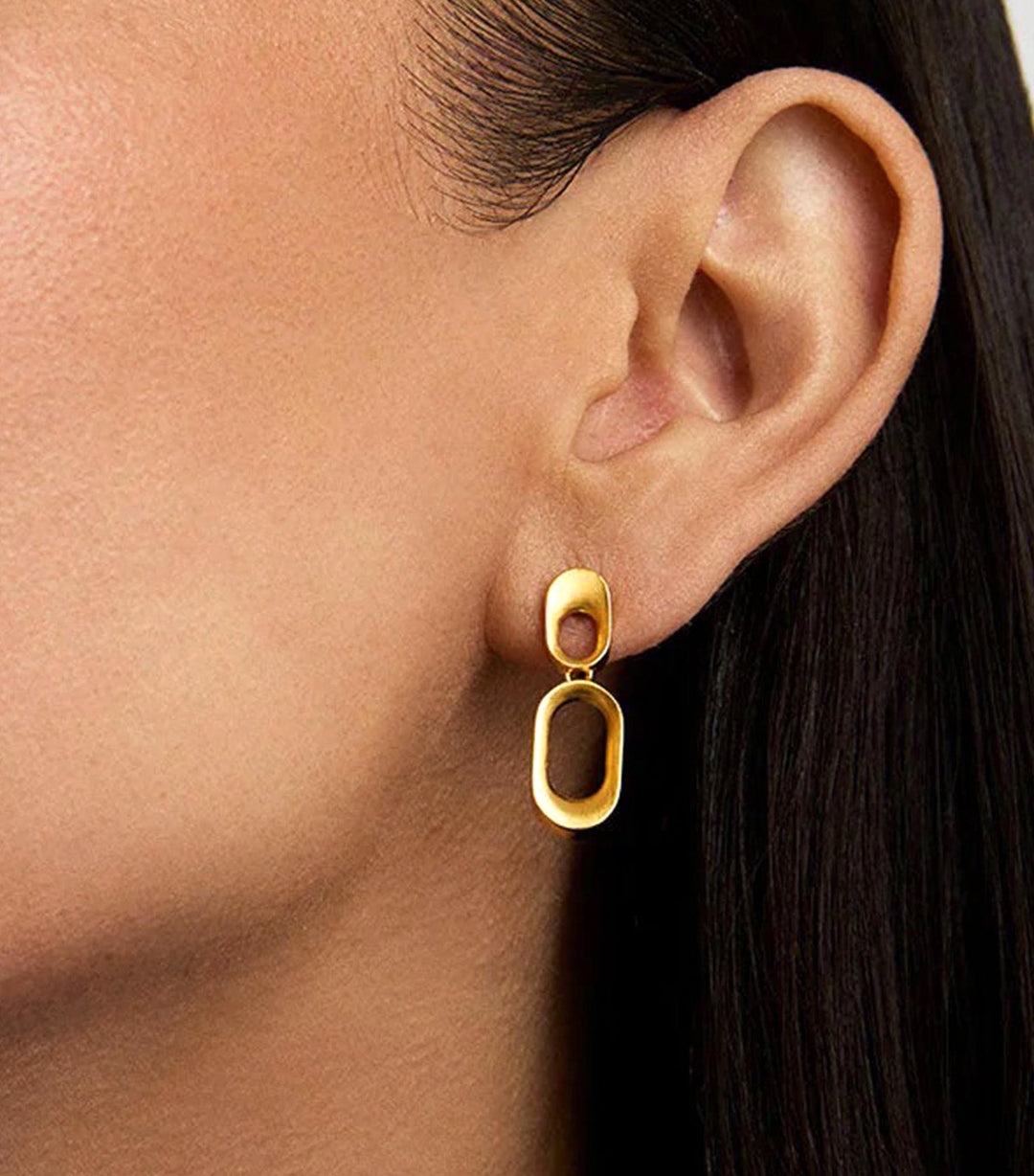 Gold drop earring with solid oval stud top and open rectangular link pendant, worn on model's ear
