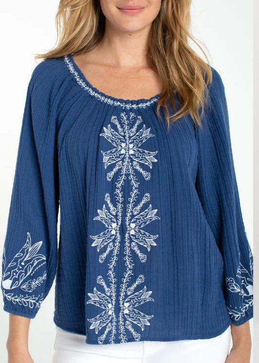 Woman wearing a blue long-sleeve top with white embroidery on a white background