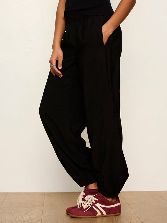 Black balloon-style harem pants with elastic waistband and tapered ankles, side view on model