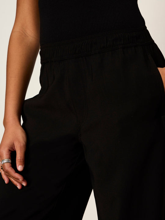 Close-up of black wide-leg pants with elastic ruched waistband, worn with black ribbed top
