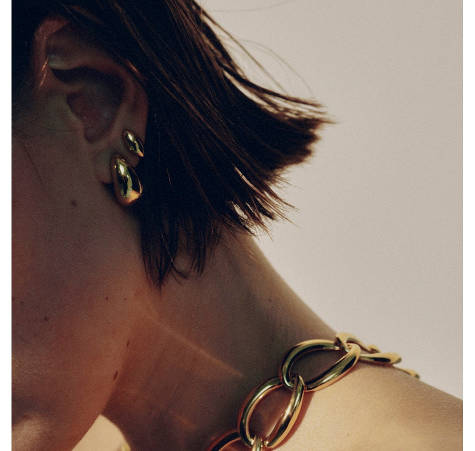 Small gold hoop earrings worn on model with short brown hair, side profile view
