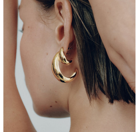Small gold hoop earrings with curved crescent moon design worn on model's ear