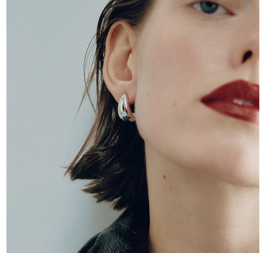 Small gold hoop earring worn on model's ear, showing curved teardrop shape