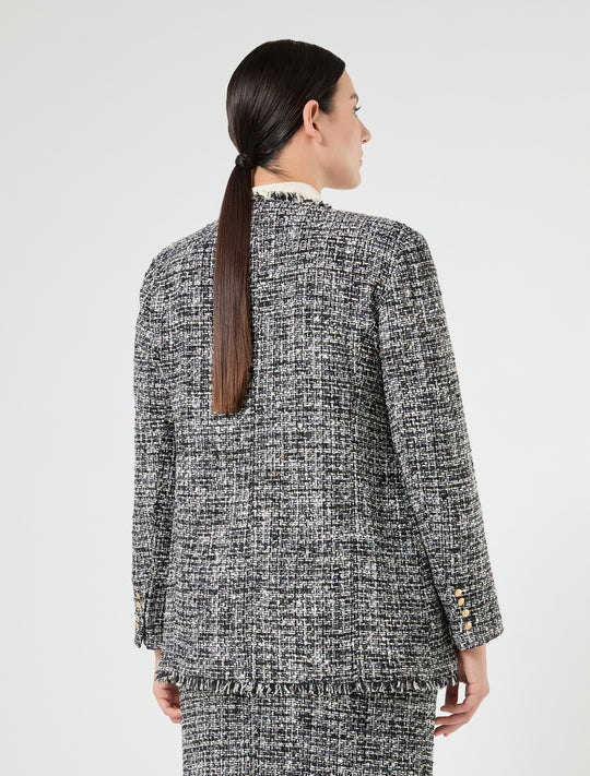 Back view of a black and white tweed boucle jacket with fringe hem and gold sleeve buttons