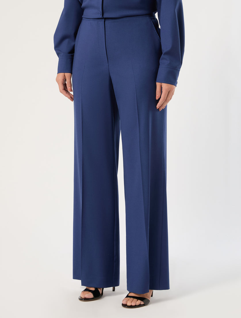 Wide-leg high-waist blue trousers with front crease detail, worn with matching blue blouse and black heels
