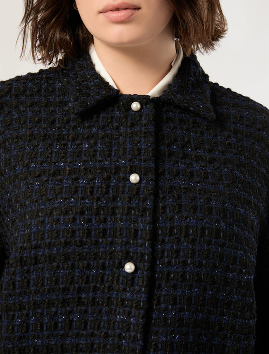Close-up of dark textured tweed jacket with pearl buttons and white collar underneath, worn by model