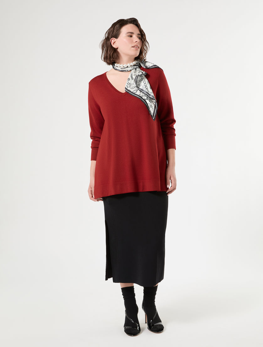 Deep red V-neck long sleeve sweater on model, paired with black midi skirt and printed scarf