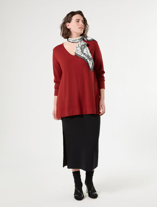 Deep red V-neck long sleeve sweater on model, paired with black midi skirt and printed scarf