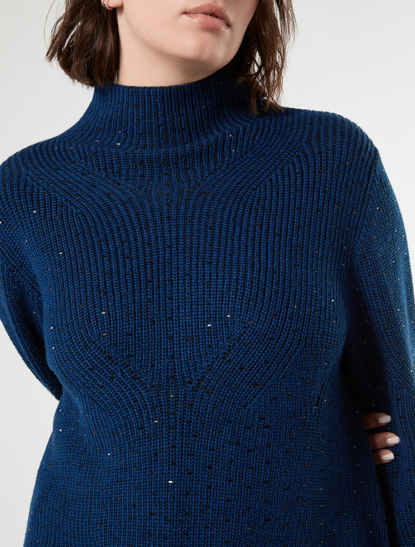 Close-up of ribbed knit mock neck sweater in blue-black with scattered metallic studs, worn by model
