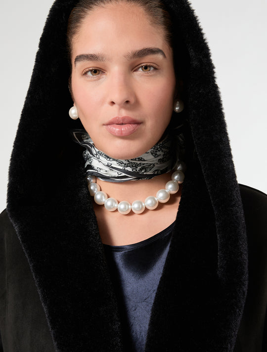 Large white pearl choker necklace and oversized pearl stud earrings worn by model with black hood