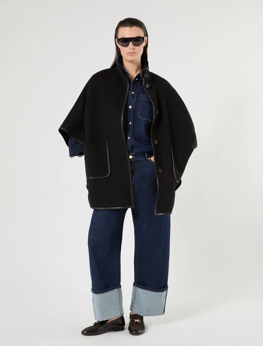 Black stand-collar cape with faux leather pockets and snap-button front; styled over denim.