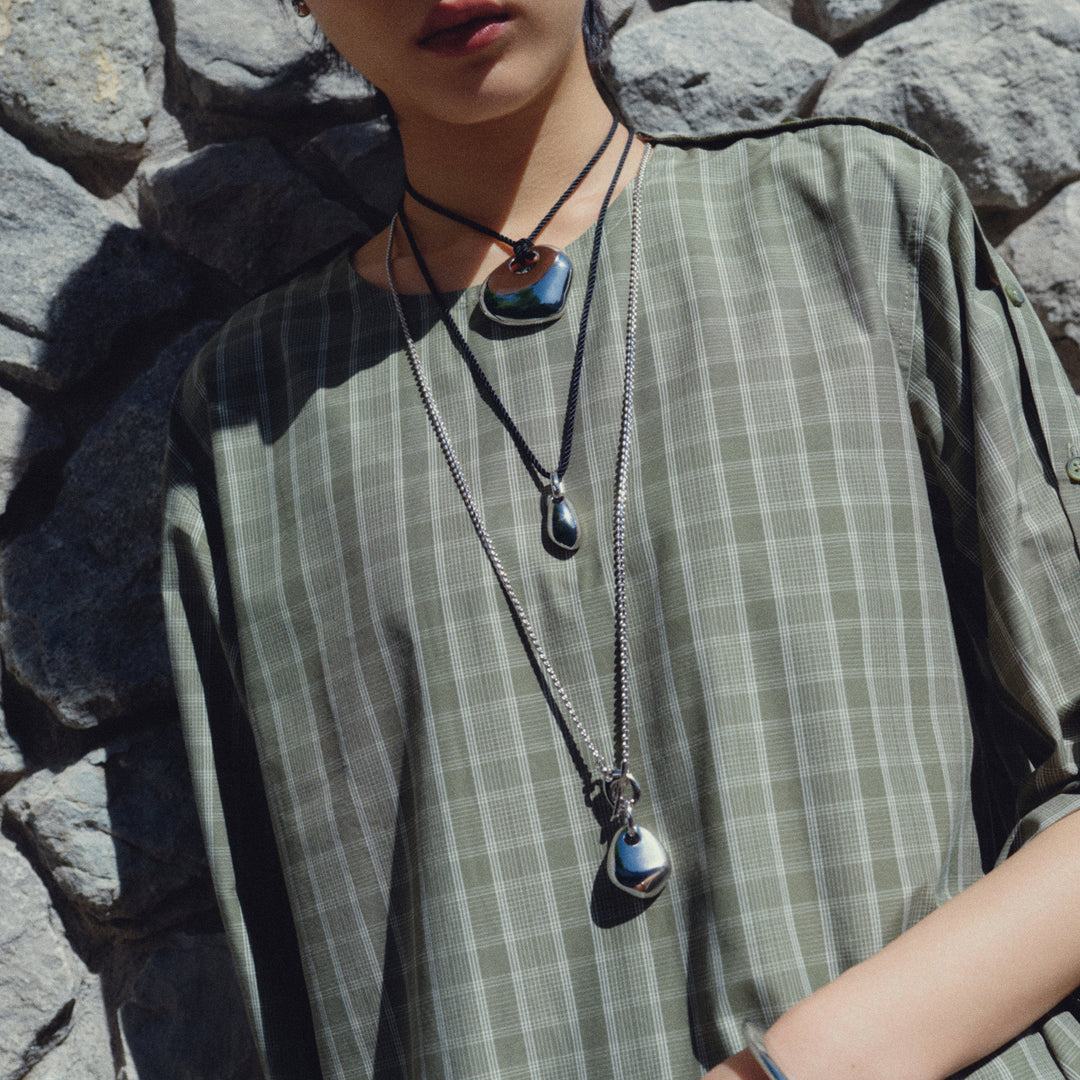 Silver metallic pendant necklace with teardrop shape worn on model with layered necklaces