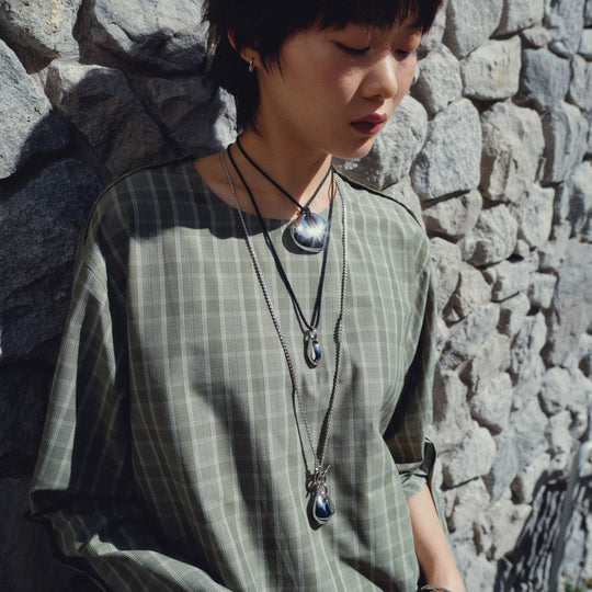 Model wearing layered silver pendant necklaces with geometric and stone details