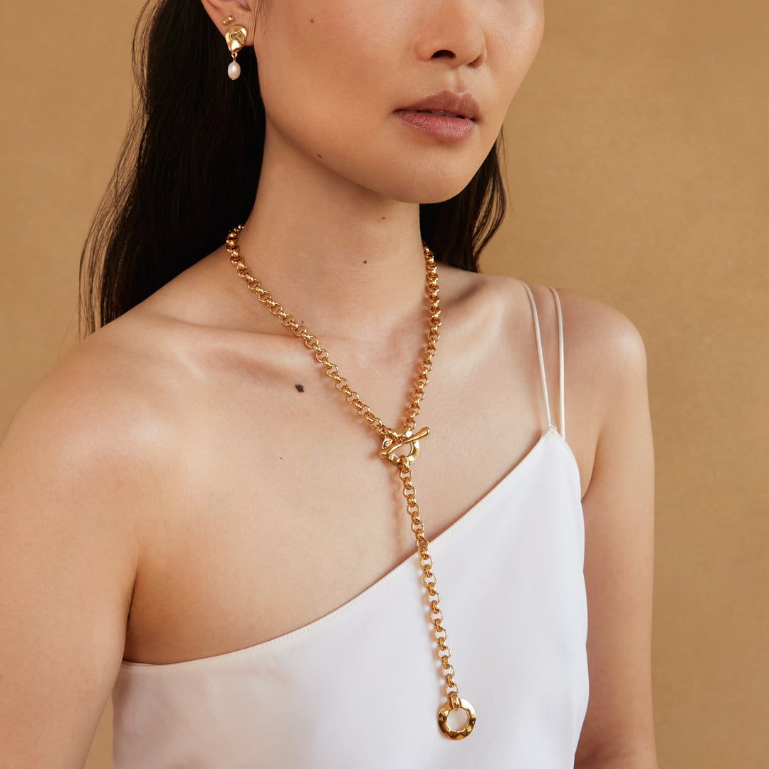 Gold chain lariat necklace with toggle closure worn by model with one shoulder top