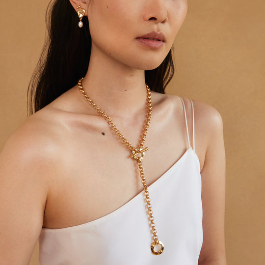 Gold chain lariat necklace with toggle closure worn by model with one shoulder top