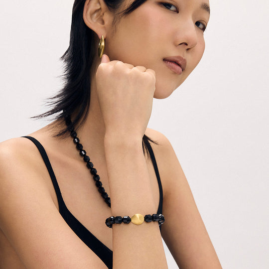 Black beaded bracelet with gold center bead on model’s wrist, adjustable cord
