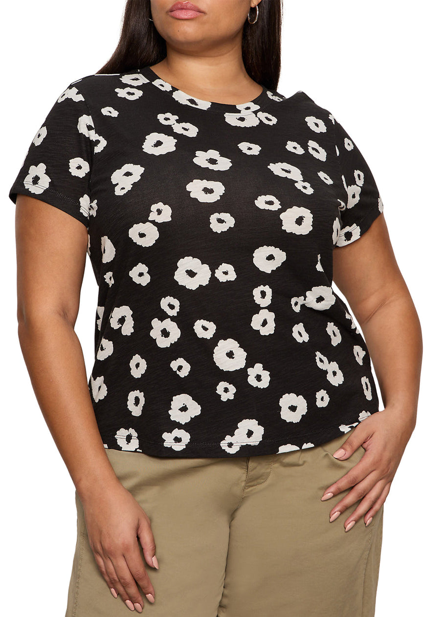 Person wearing a black t-shirt with white floral pattern and beige pants on a plain background