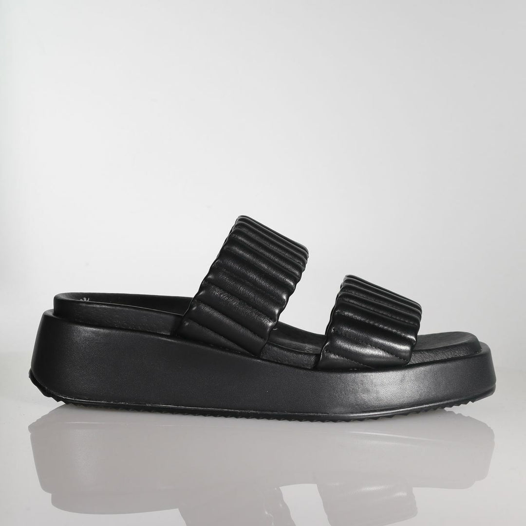 Black leather platform slide sandal with quilted straps on reflective surface