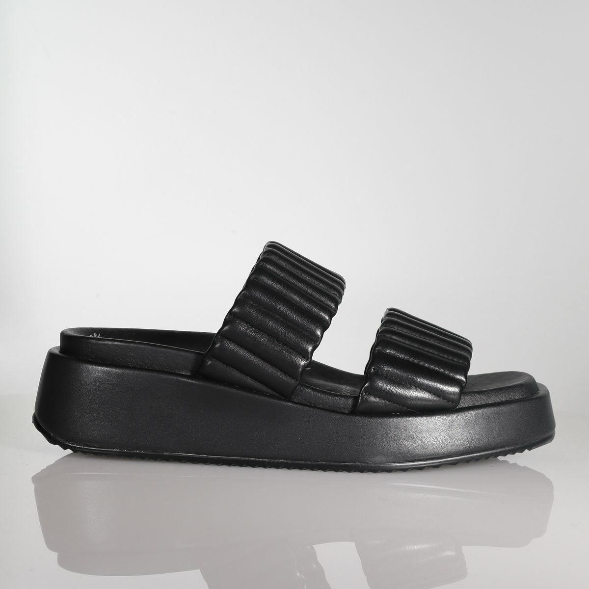 Black leather platform slide sandal with quilted straps on reflective surface