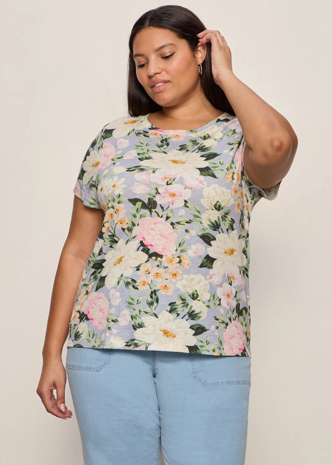 Woman wearing a floral top and light blue jeans against a plain background