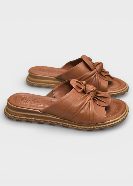 Pair of brown sandals with bow details on a light gray background