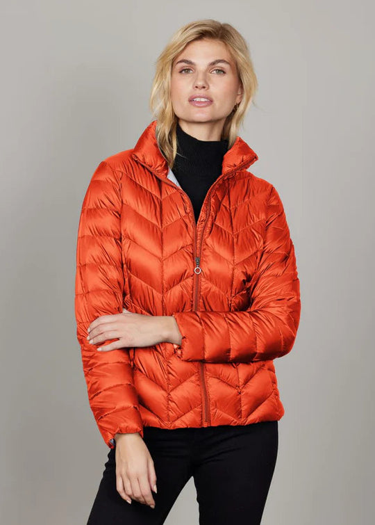 Woman wearing an orange puffer jacket against a gray background