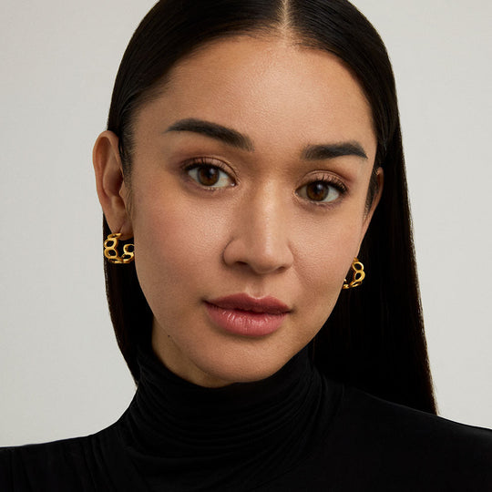 Gold chain-link huggie hoop earrings worn by a model, close-up view showing both ears