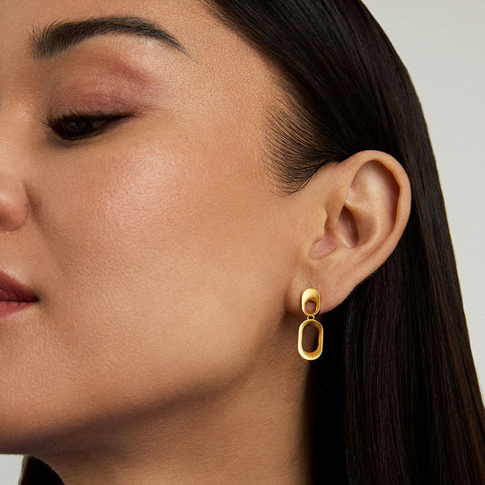 Gold drop earrings with solid stud top and open oval pendant, worn on model's ear