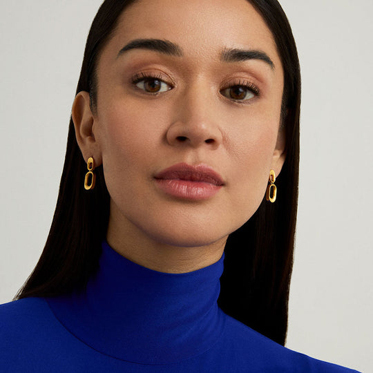 Model wearing gold double oval link drop earrings with blue turtleneck, close-up side view