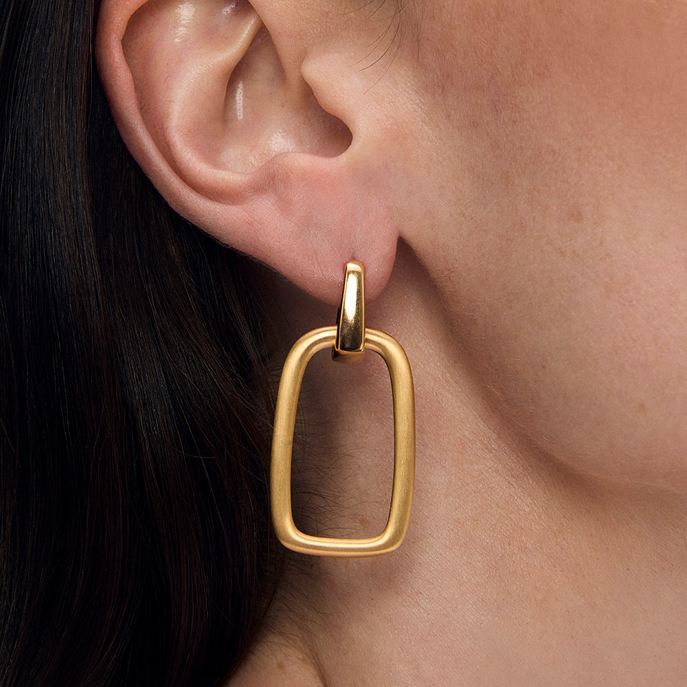 Gold drop hoop earring with rectangular open frame pendant worn on model's ear