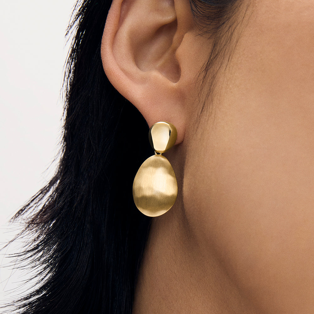 Gold drop earring with small stud top and large oval pendant, worn on model's ear