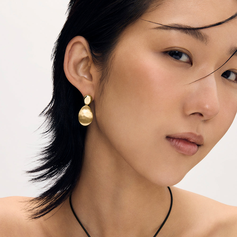 Gold double-disc drop earring with matte finish worn by model, close-up side view