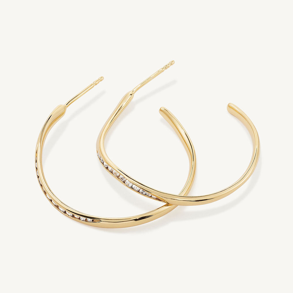 Pair of large gold hoop earrings with channel-set white crystal stones along the inner edge
