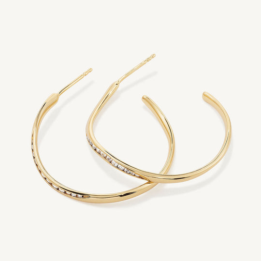 Pair of large gold hoop earrings with channel-set white crystal stones along the inner edge