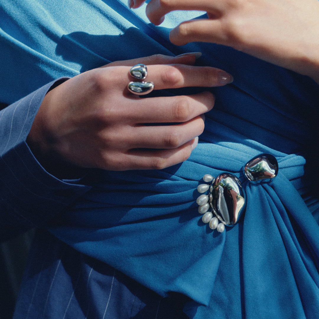Silver brooch with pearl accents worn on blue fabric, styled with matching silver rings