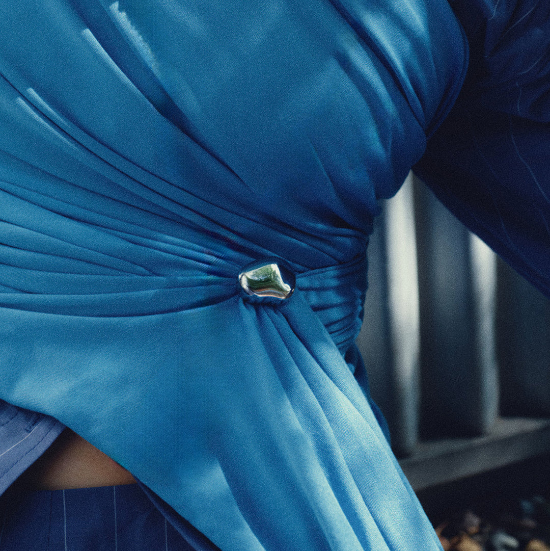Silver brooch worn on blue draped fabric, geometric curved design visible