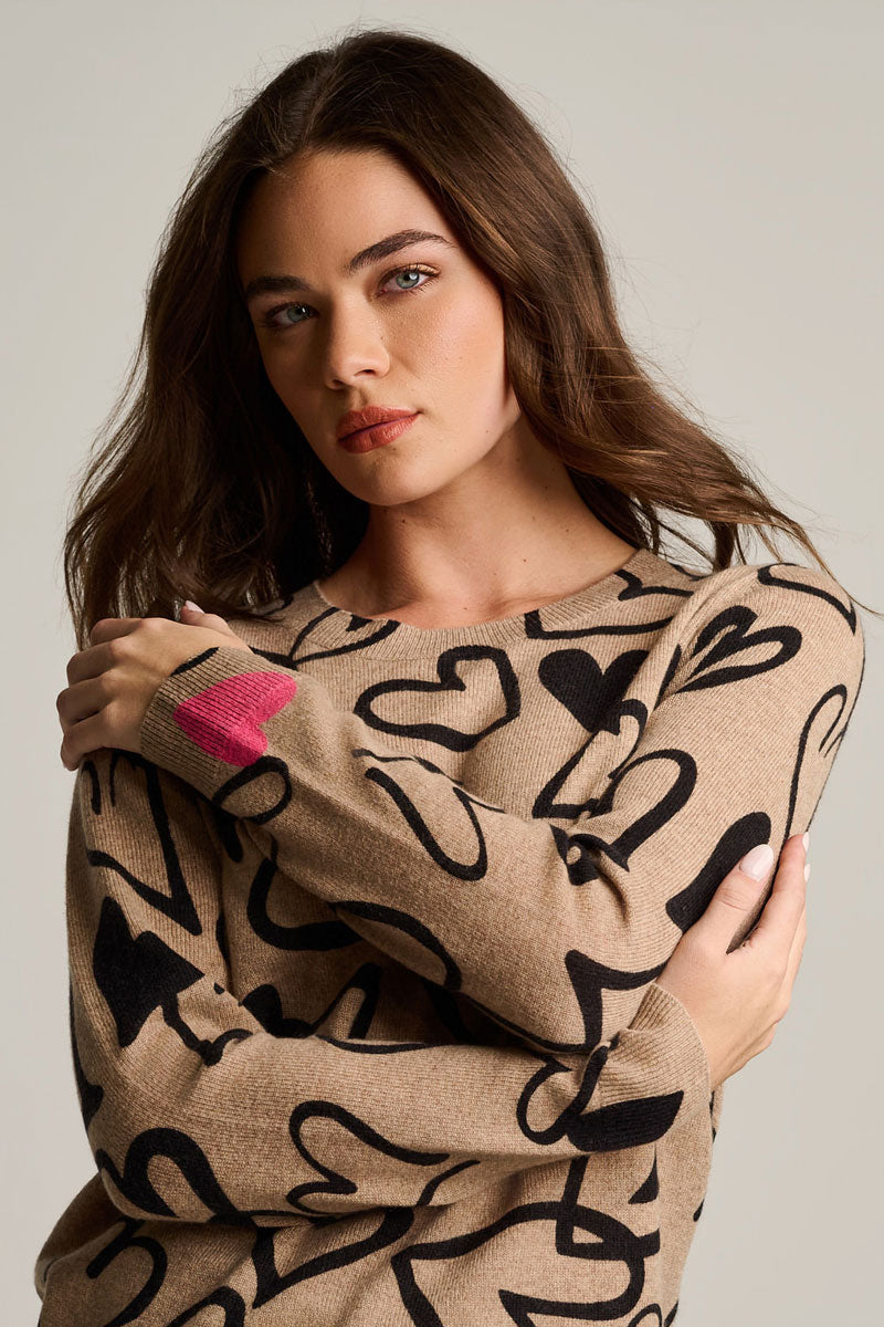 Cashmere heart-print sweater close-up, biscuit beige with black hearts and pink heart detail
