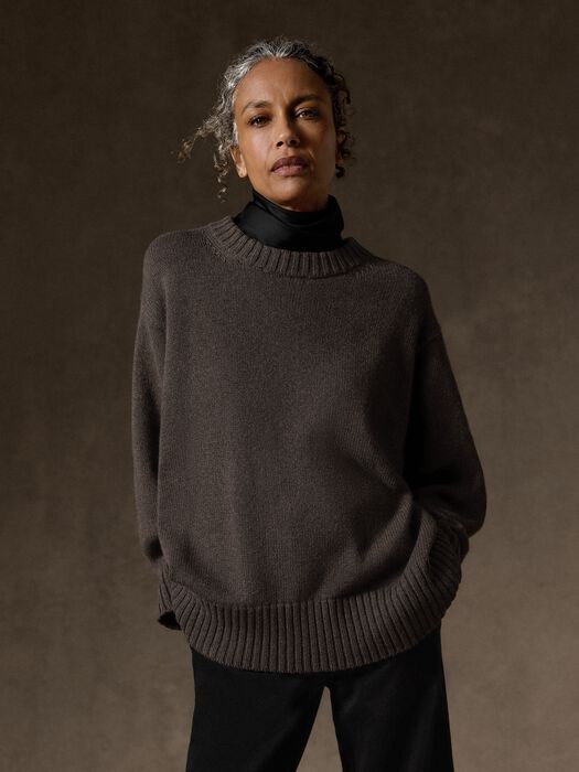 Oversized crew neck knit sweater in dark taupe, worn over black turtleneck, front view on model