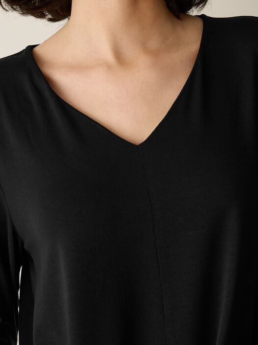 Close-up of a black V-neck long-sleeve knit top with center seam detail, worn by a model