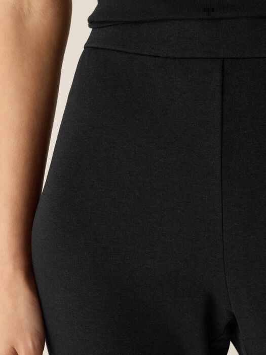 Close-up detail of high-waisted black knit kick pants with seam detailing, worn by model