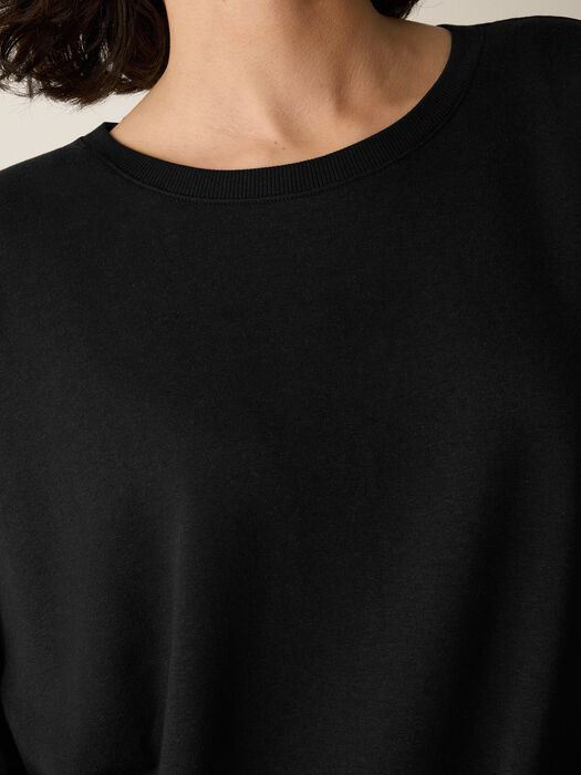 Close-up of a black crew neck sweatshirt with ribbed neckline, worn by a model