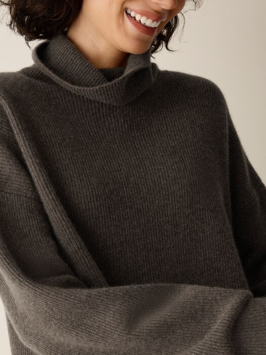 Close-up of a ribbed turtleneck cashmere sweater in dark charcoal gray, worn by smiling model